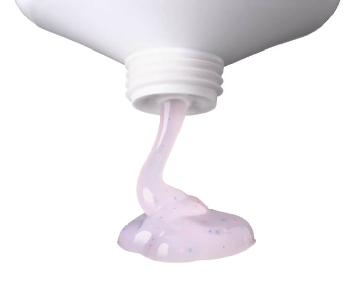 Pink skincare product dispensing from white tube showing plastic microbeads in formula
