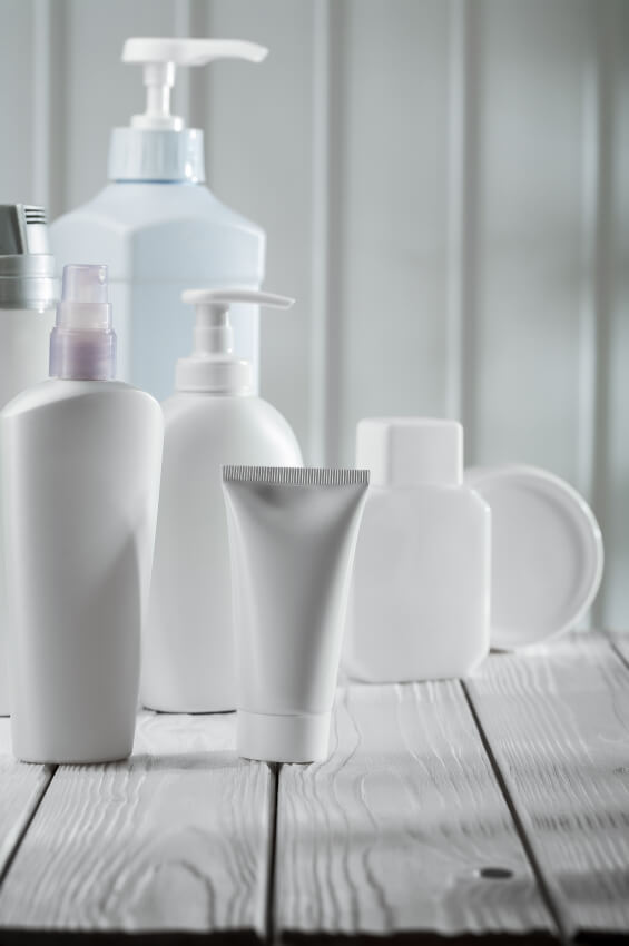 Collection of white skincare bottles and pump dispensers arranged on wooden surface in clean, minimalist bathroom setting