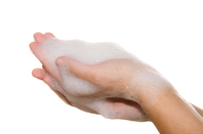Hands creating rich foam with gentle cleanser, demonstrating sulfate-free cleansing for sensitive skin