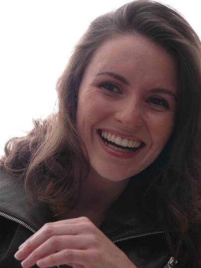 Confident woman with radiant glowing skin smiling warmly outdoors in natural light