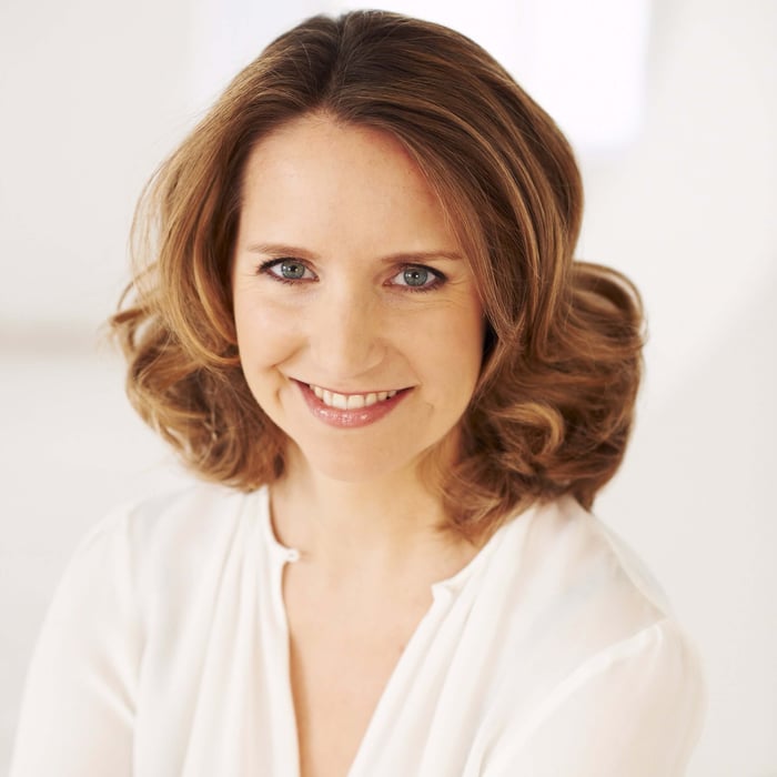 Smiling woman with radiant skin and wavy brown hair wearing white blouse for age confidence campaign