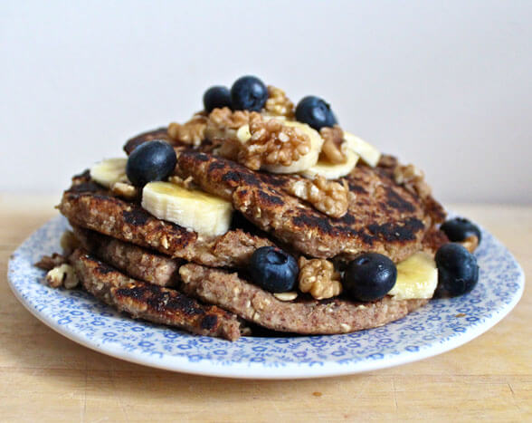 Stack of healthy buckwheat pancakes topped with fresh blueberries, banana slices and crushed walnuts on decorative plate