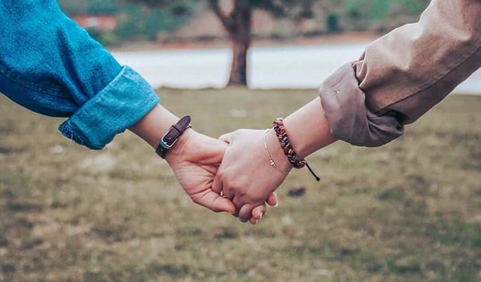 Two people holding hands outdoors, showing connection and support between women