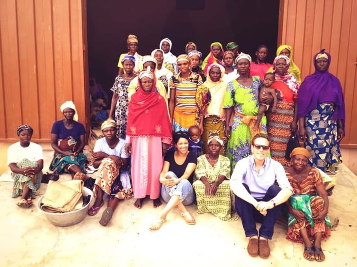 Pai Skincare founder with shea butter cooperative women in traditional West African dress gathered outside building