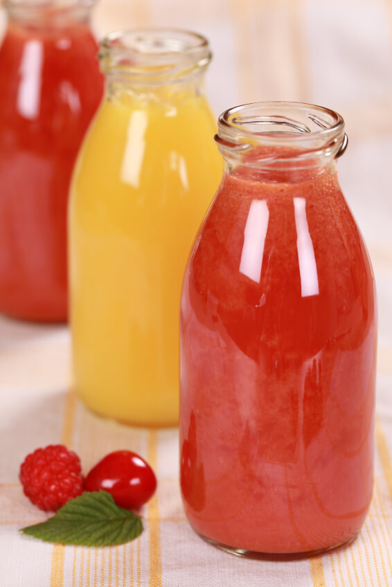 Glass bottles of fresh red and yellow fruit smoothies on wooden surface with raspberries and mint garnish