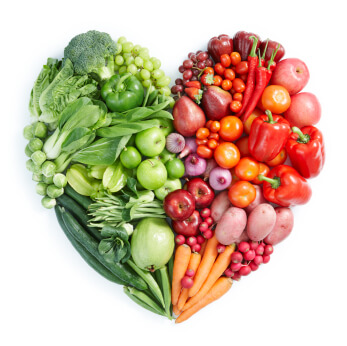 Heart-shaped arrangement of fresh fruits and vegetables in gradient from green to red, representing nutritious foods for healthy skin