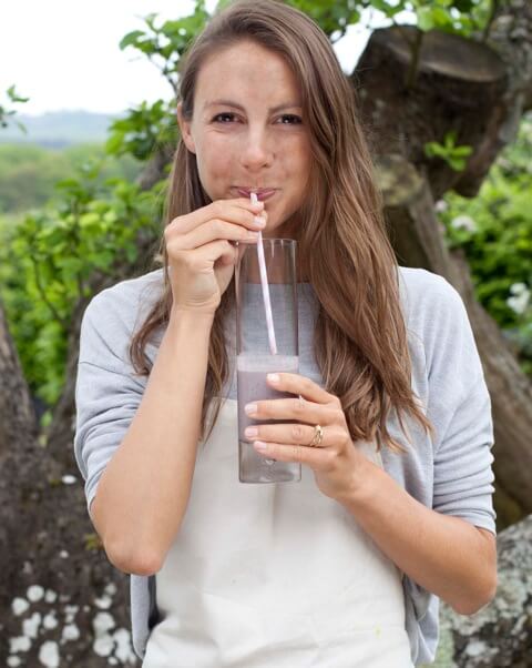Woman drinking green smoothie outdoors with natural tree background, promoting healthy organic lifestyle