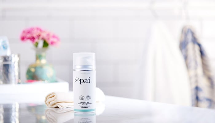 Pai Camellia & Rose Gentle Hydrating Cleanser bottle in elegant bathroom setting with pink flowers and soft lighting