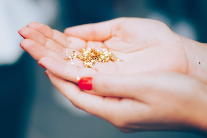 Cupped hands with red nail polish holding golden glitter flakes, representing nail polish ingredients and beauty choices