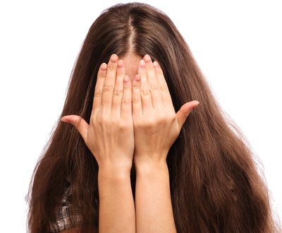 Woman with long brown hair covering her face with both hands, expressing distress about skin concerns