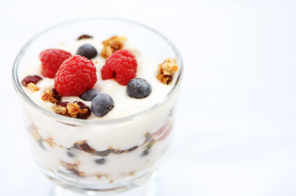 Glass bowl of yogurt topped with fresh raspberries, blueberries and nuts on white background
