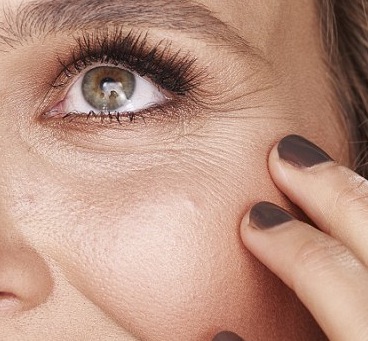 Close-up of woman's eye area showing fine lines and crow's feet with finger touching under-eye skin
