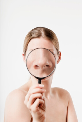 Woman holding magnifying glass over nose area to examine skin closely