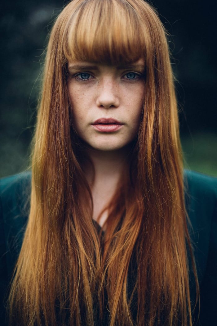 Young woman with freckles and long red hair looking directly at camera with clear skin