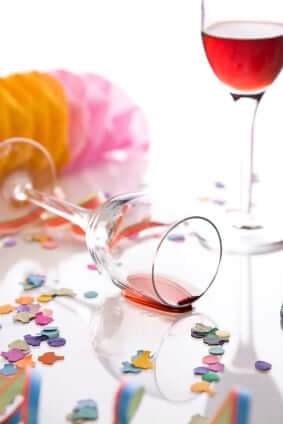 Fallen wine glass with spilled red wine and colorful party confetti scattered on white surface