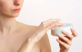 Woman applying moisturiser from white jar to face, demonstrating anti-aging skincare routine