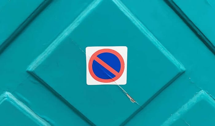 No parking sign on turquoise geometric surface representing banned cosmetic ingredients DEG and Vitamin K