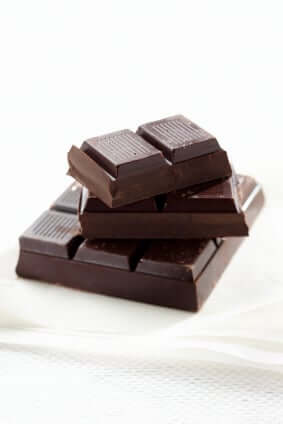 Stack of dark chocolate squares with ribbed texture on white surface