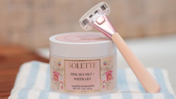 pink sea salt and water lily sugar scrub paired with a pink shaving razor and a white and blue hand towel