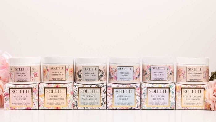 a collection of shea body butters and their matching sugar scrubs set on a white background with flowers all around