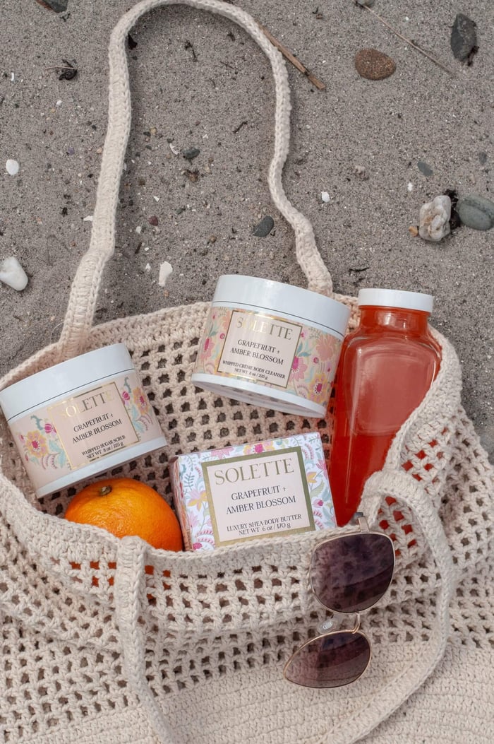 summer self care with body care products in a beach bag on the sand