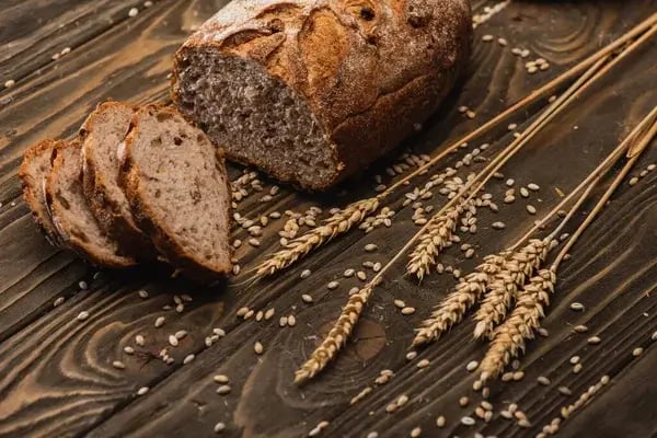 Sliced homemade no-knead rye bread with whole grain stalks on a wooden table