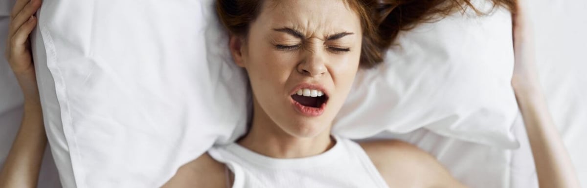 Female Presenting Person, who's vagina hurtlaying in bed pulling a face like she is uncomfortable or in pain.. 