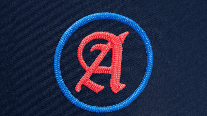 A simple, circular patch with a red letter "A" inside a blue ring, sewn onto a dark navy blue fabric background