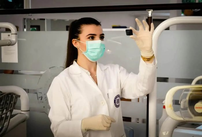 a lab worker looking at a sample wearing protective gear and an embroidered lab coat