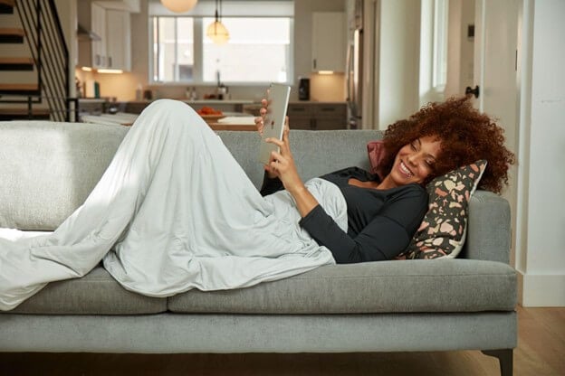 Woman on the Couch Reading a Tablet and Snuggled in a Temperature Regulated Sheet
