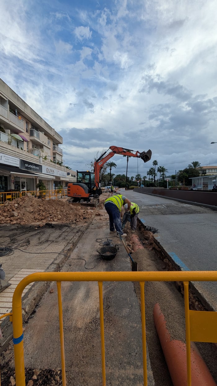 Mini excavator and two workers laying orange ducting in a trench on Avenida Rei Jaume I