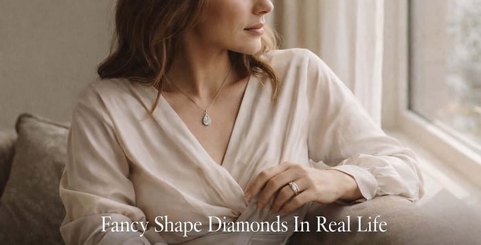 Woman in soft window light wearing a pear-shaped diamond pendant and emerald-cut diamond ring with text overlay reading Fancy Shape Diamonds In Real Life