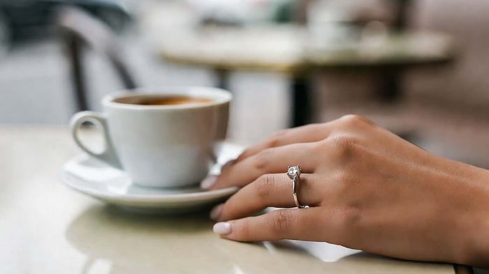 Contemporary engagement rings, evoke an emotional response, here a woman is wearing a refined slitiare diamond ring in a coffee shop, with golden hour lighting and high resolution.