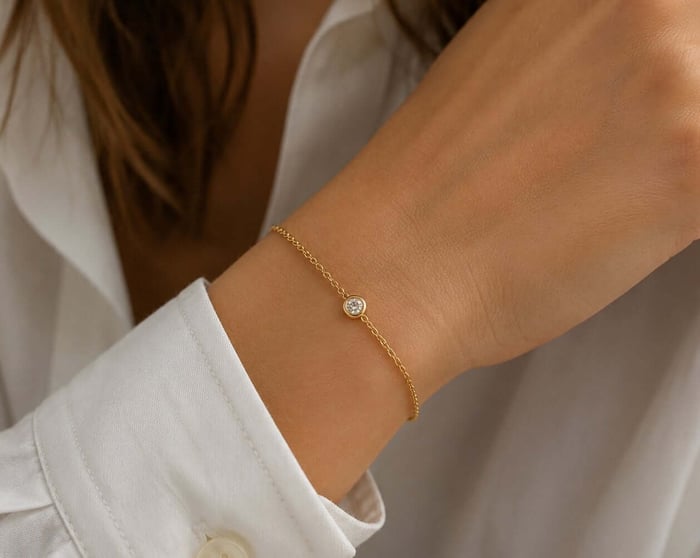 Delicate yellow-gold bracelet with one bezel-set natural diamond worn beside a white shirt cuff