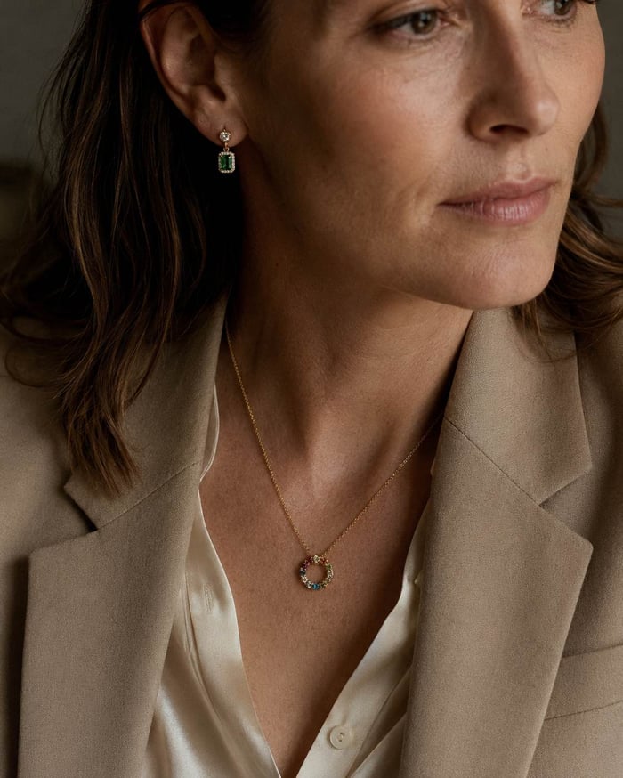 Woman wearing a multicolour sapphire pendant and emerald earrings with natural diamond accents.