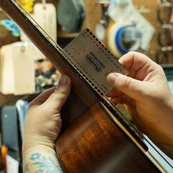 Technician measuring string height with a string action gauge during a guitar inspection at The Acoustic Shoppe