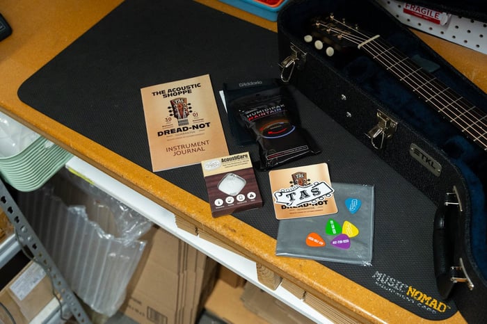 Dread-Not case candy laid out beside an open guitar case: instrument journal, humidity pack, sensor and TAS picks