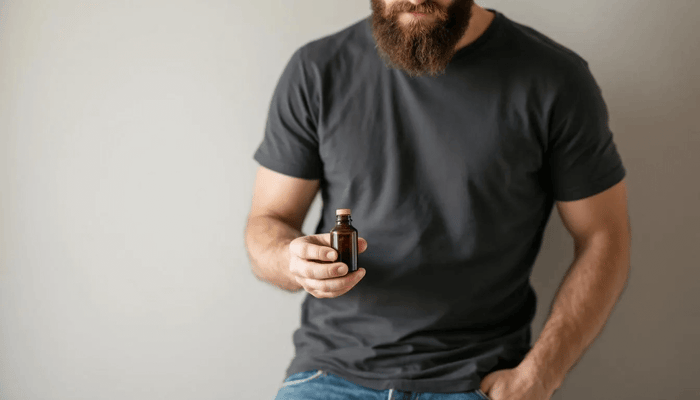 A hand holds a bottle of natural beard oil, ready to apply a few drops to nourish and soften facial hair. The oil blend, featuring ingredients like jojoba oil and sweet almond oil, promotes healthy beard growth while soothing the skin underneath.