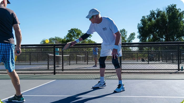 Pickleball player wearing a knee compression sleeve demonstrates balance and proprioception during play on an outdoor court.