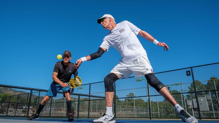 Athlete with tennis elbow in pickleball wearing an elbow compression sleeve on an outdoor court.