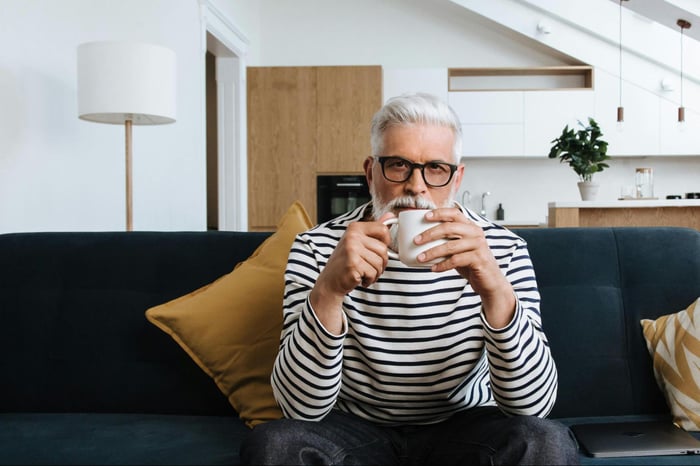 older gentleman drinking coffee on black sofa