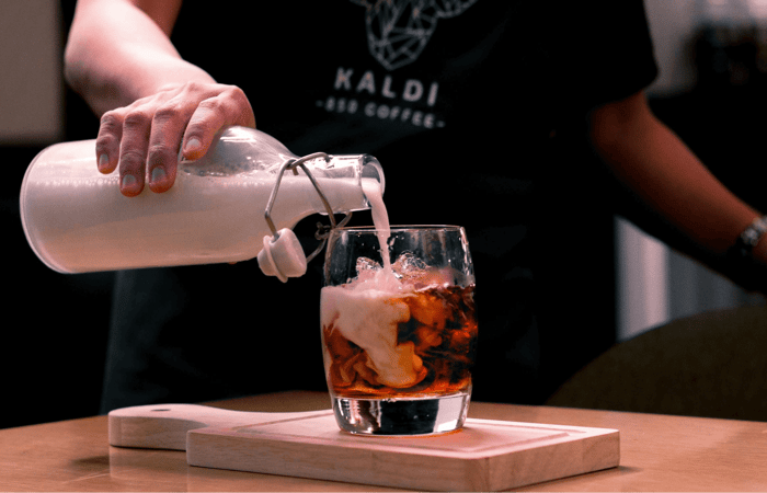person pouring milk on iced coffee