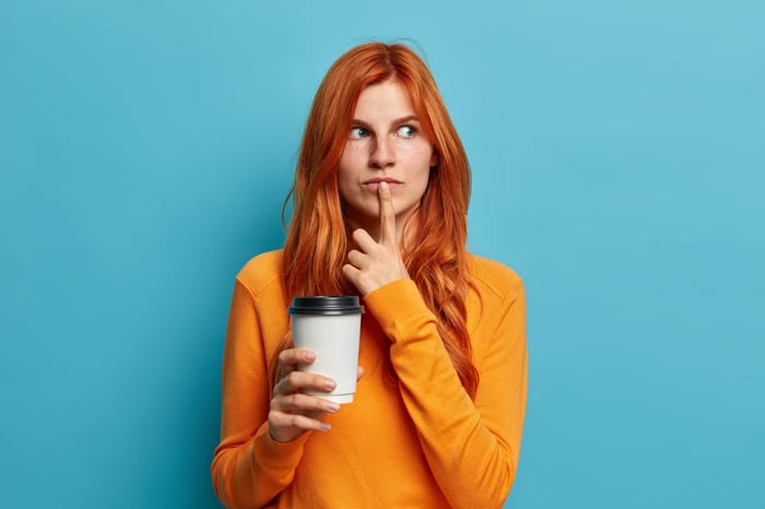 redhead woman thinking with finger on lips while holding coffee cup with other hand.