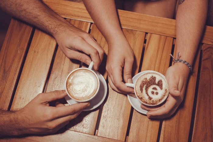two people holding their coffee cups on a wooden table