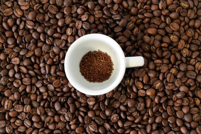 cup with instant coffee surrounded by whole roasted beans