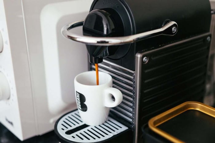 Black espresso machine brewing coffee into white cup.
