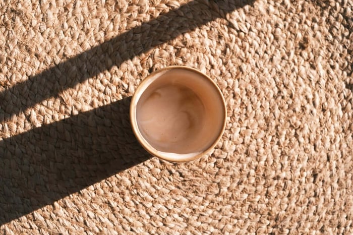 Empty cup casts shadow on woven mat.