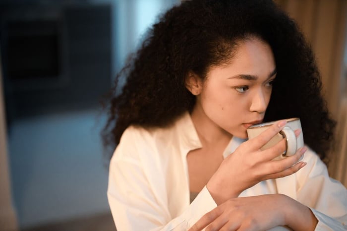 Woman holding cup of coffee, gazing to side.