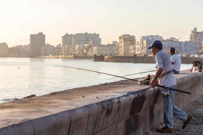 Angler fishing alone at the end of a wooden pier, rod extended over calm seawater during a quiet day.