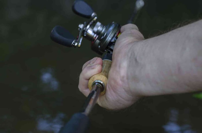 Fisherman gripping a baitcasting reel for precision casting
